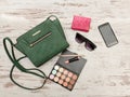 Green female bag, phone, eyeshadow palette, phone, sunglasses and lipstick on a wooden background. Royalty Free Stock Photo