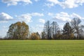 A green field and trees under a clear blue sky and white clouds. Autumn landscape on a bright sunny day Royalty Free Stock Photo