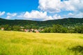 Green field under the bright sunlight  on the background of rural houses and greeny mountain Royalty Free Stock Photo