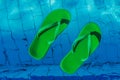 Green flip flops floating in the swimming pool, top view