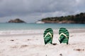 Green flip flops in the white sandy beach near sea waves, nobody. Summer vacation concept with blue water. Relax, vacation on Royalty Free Stock Photo