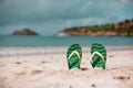 Green flip flops in the white sandy beach near sea waves, nobody. Summer vacation concept with blue water. Relax, vacation on Royalty Free Stock Photo