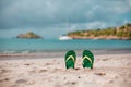 Green flip flops in the white sandy beach near sea waves, nobody. Summer vacation concept with blue water. Relax, vacation on Royalty Free Stock Photo