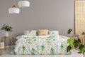 Green flower in vase on nightstand next to king size bed with floral bedding and peach colored pillow, copy space on the empty