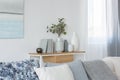 Green flowers in grey vase next to books on wooden console table in bright living room interior