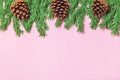 Green foam Christmas tree branch border with cones on the pink background flat lay, top view. Handmade New Year decor with copy
