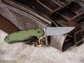 Green folding EDC knife near a vintage leather bag