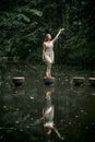 In a green forest, a young woman in a macrame dress stands on a concrete circle.