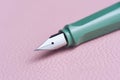 Green fountain pen lies pink leather tabletop desk.