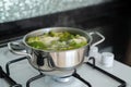 Green fresh broccoli is cooked in water in metal silver saucepan on gas white stove.