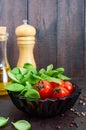 Green fresh leaves of organic basil and small ripe tomatoes, oil and pepper on a wooden background Royalty Free Stock Photo