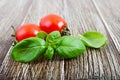 Green fresh leaves of organic basil and small ripe tomatoes on a wooden background Royalty Free Stock Photo