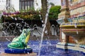 Green frog statue pours water out of its mouth into colorful fountain