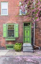 Green front door entrance and old-style window with shutters of a red brick house in spring. Royalty Free Stock Photo