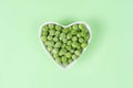 Green frozen peas in a white heart-shaped bowl on light green background. Concept love vegetables, vegetarian food. Diet Royalty Free Stock Photo