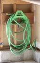 Green garden hose sloppily hung on a rack inside an unfinished wall in a garage or a shop