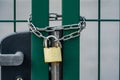 Green gate secured with a strong chain and a generic padlock, object closeup. Security and safety of premises, locked out lot,