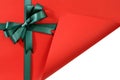 Green gift ribbon bow on plain red background paper, corner folded open showing white copy space inside Royalty Free Stock Photo