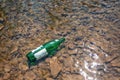 Green glass bottle lying in the shallow water of the river. Concept of environmental pollution Royalty Free Stock Photo