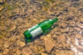 Green glass bottle lying in the shallow water of the river. Concept of environmental pollution. Close up Royalty Free Stock Photo