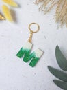 green glitter letters with beads. Golden keychain on white paper background with dried flowers. Top view. Resin craft