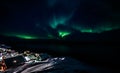 Green glowing of Aurora Borealis with shining stars over the fjord and Inuit village huts, Nuuk, Greenland
