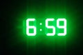 Green glowing digital clocks in the dark show 6:59 time