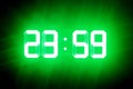 Green glowing digits in the dark show 23:59. Time is one minute to midnight