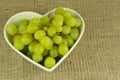 Green grapes in a heart shaped bowl on a rustic background