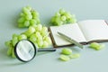 Green grapes, magnifying glass, pen and notebook on light green background. Checking the quality of grapes. Selection of grapes