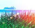 Green grass with a blurried unfocused cruise ship sailing away on sunset horizon. Vacation conception. RGB toned with a colorful l Royalty Free Stock Photo