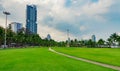 Green grass field, pedestrian road and coconut trees at the city park beside the sea. Modern building Royalty Free Stock Photo