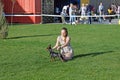 On green grass, a girl sitting on her knees, holding a ponytail of the breed Prague Ratter