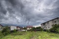 Green grass and houses under dark sky with clouds before storm