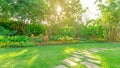 Green grass lawn in a garden with random pattern of grey concrete stepping stone , Flowering plant, shurb and trees on backyard