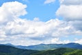 Green grass, mountains peaks covered with forest and cloudy blue sky. Summer mountain landscape Royalty Free Stock Photo