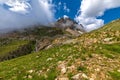 Green grass on the slope and mountain peak under beautiful sky in Italy.