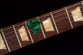 Green guitar pick on the fingerboard and dark