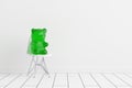 Green gummy bear sitting on a chair in the house interior with white wall and floor