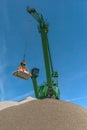 Green harbor crane pours sand and gravel onto a hill