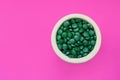 Green hawaiian spirulina in tablespoons pills on pink background. Super food, healthy lifestyle, Royalty Free Stock Photo