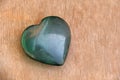 Green heart made of natural stone jade. A heart shaped stone lies on a brown or beige background. Love talisman, zen, spa