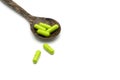 Green herbal capsules, medaical pills in wooden spoon on white. Royalty Free Stock Photo