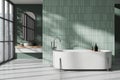 Green home bathroom interior with bathtub and sink, window and empty tile wall Royalty Free Stock Photo