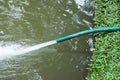 Green hose with water  drain spraying on the pond Royalty Free Stock Photo