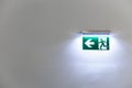 Green illuminated emergency exit sign on a white wall of a building Royalty Free Stock Photo