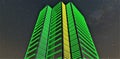 Green illumination of the awesome office building. Yellow glowing inserts. Bottom view against the starry sky. 3d rendering