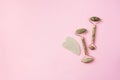 Green jade face roller and gua-sha scraper for facial acupuncture massage on pink background. Copy space. Skin care, face