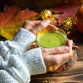 Green Japanese matcha tea with foam in transparent Cup on wooden table in autumn still life. Women`s hand with long white sweater