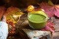 Green Japanese matcha tea with foam in transparent Cup on wooden table in autumn still life. Women`s hand with long white sweater